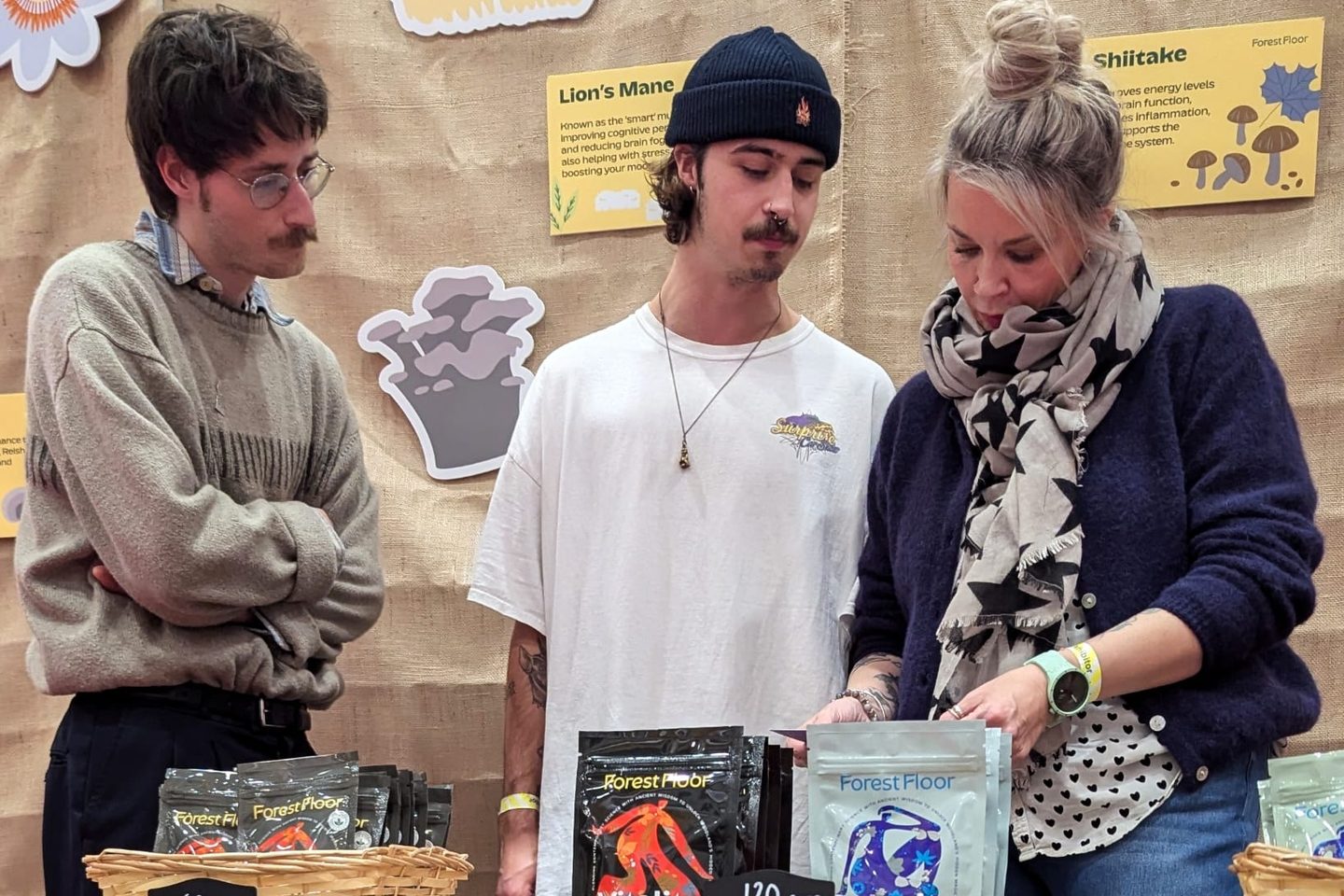 Jade at a Forest Floor stand at a live event, showing Vitality and Serenity pouches to two visitors